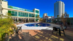 Ein moderner Innenhof eines Hotels mit Swimmingpool, Außenmöbeln und einem Gebäude mit Glasfassade.
