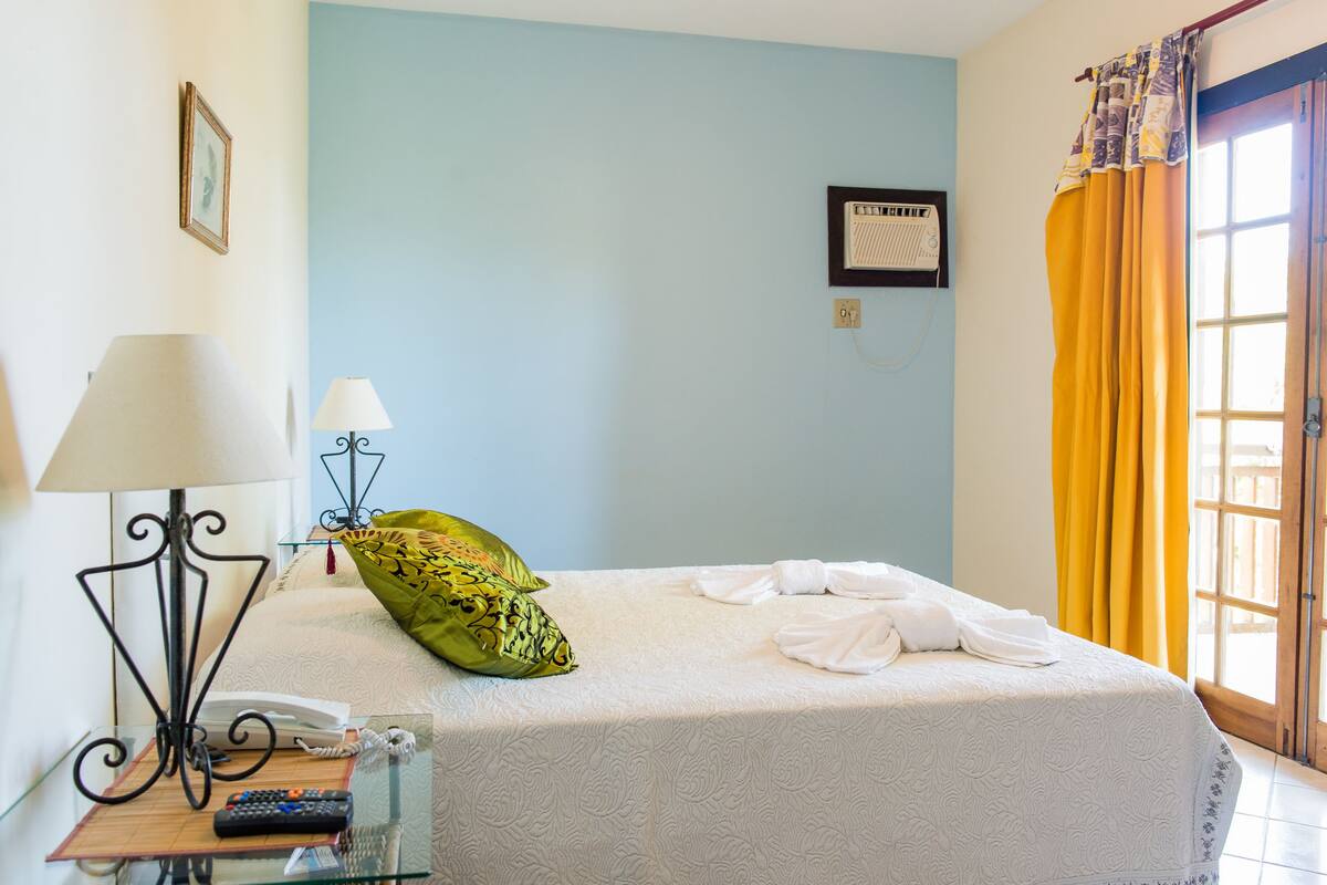 A hotel room with a bed, a bedside table with a lamp, a remote control, and a telephone.