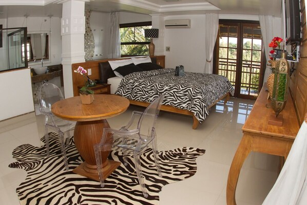 A bedroom with a zebra-patterned rug, a wooden dining table with chairs, a bed with a zebra-patterned bedspread, and a bathroom with a large mirror and sink.