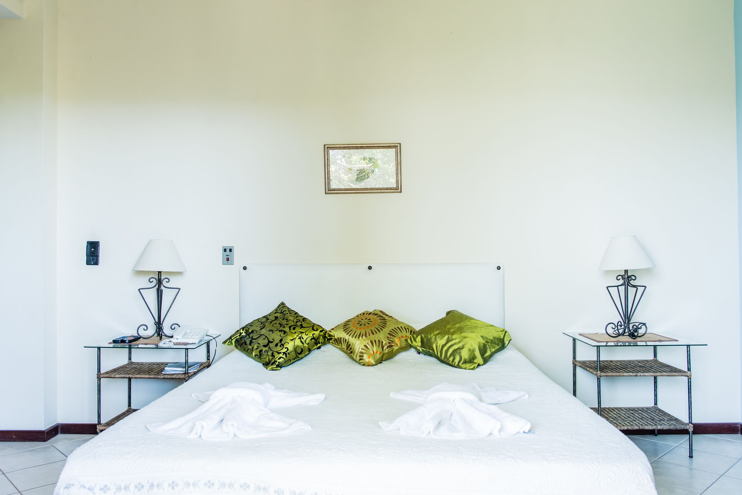Una habitación de hotel con cama, dos mesitas de noche, dos lámparas y tres almohadas decorativas.