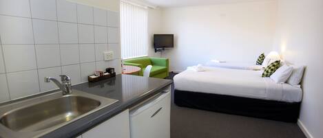 A hotel room with a kitchen area, a bed, and a television.