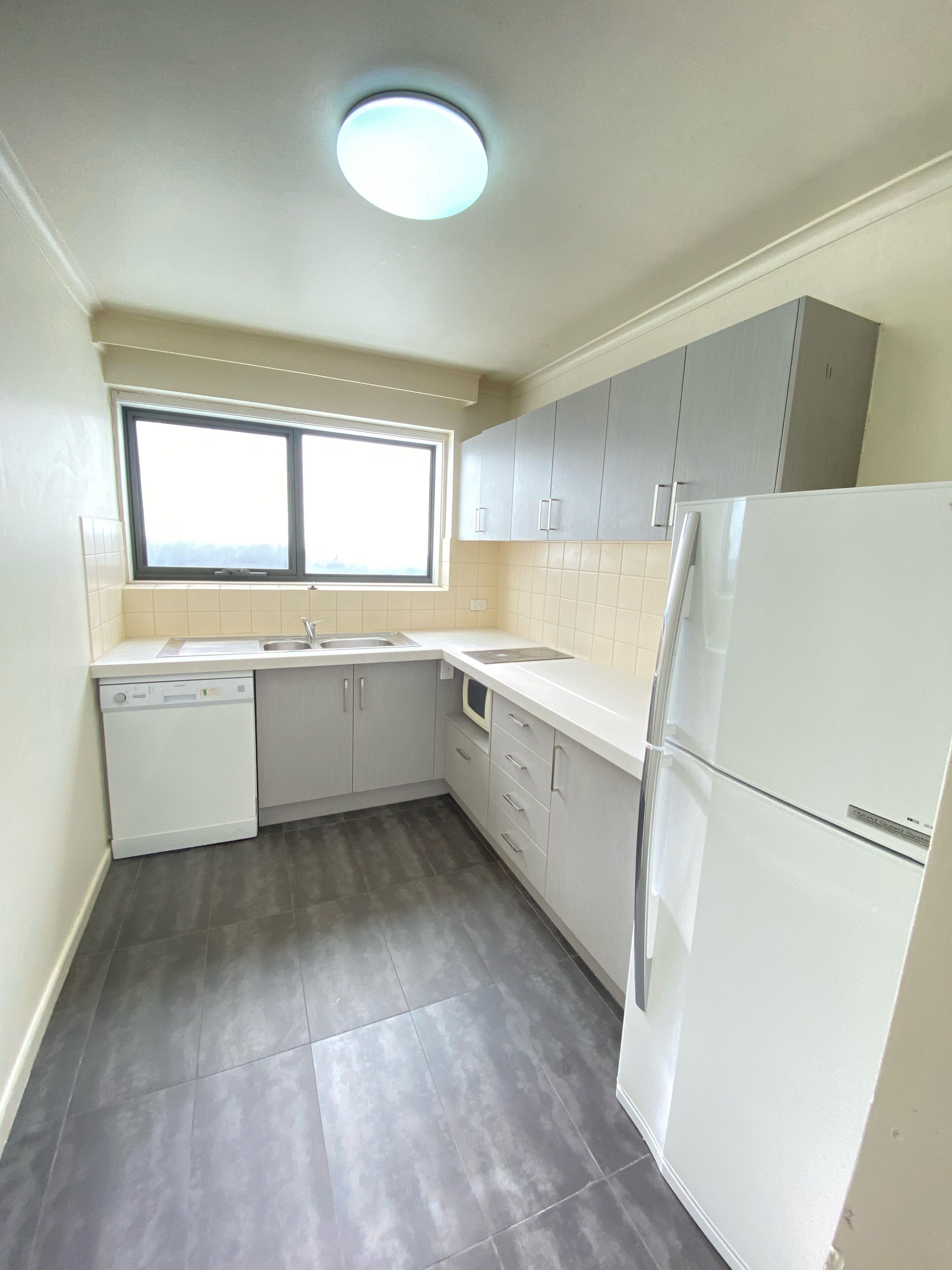 A compact kitchen with a dishwasher, a refrigerator, and a window providing natural light.