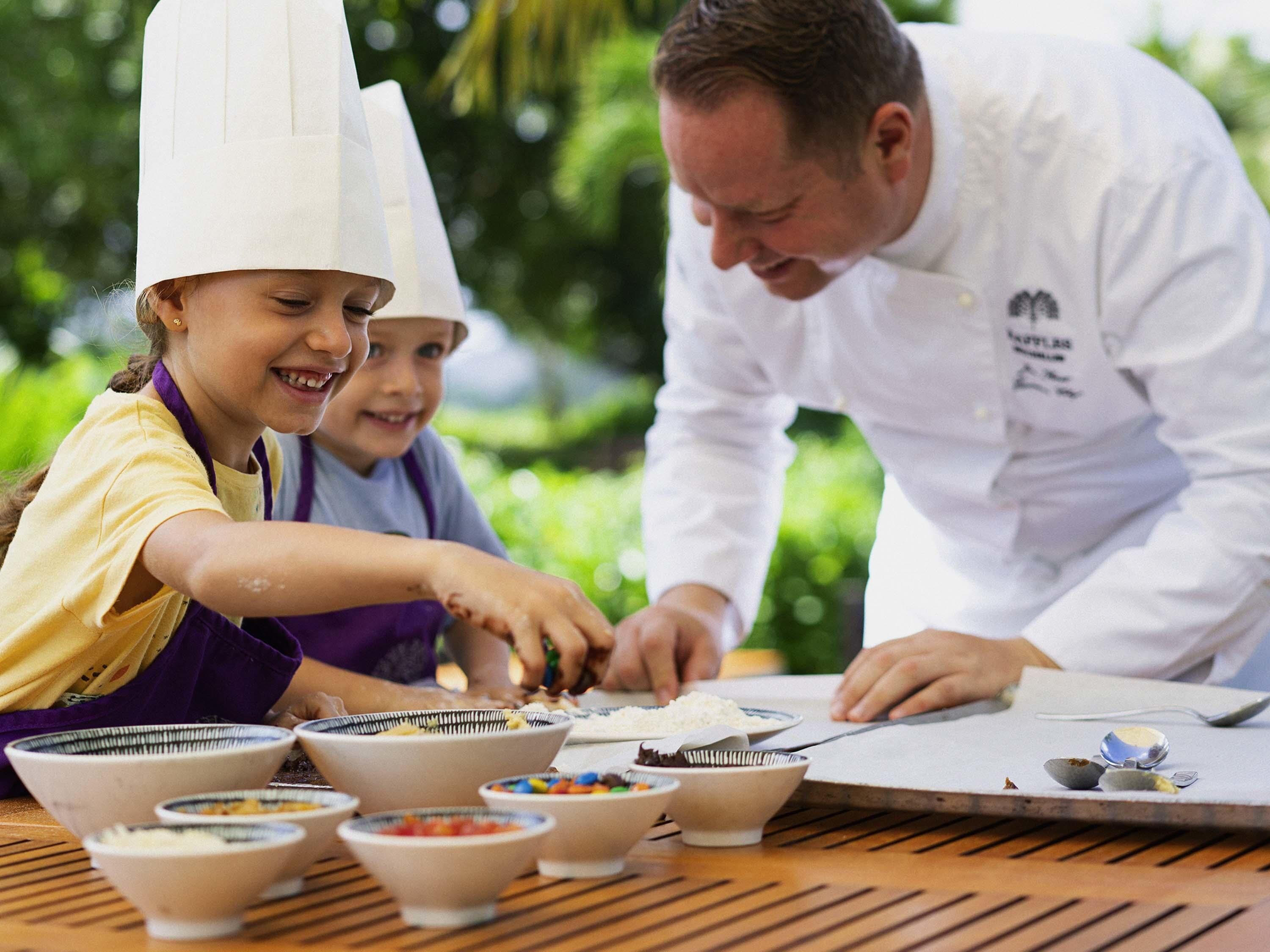 A group of people wearing chef hats, preparing food outdoors with various bowls and utensils on a table.