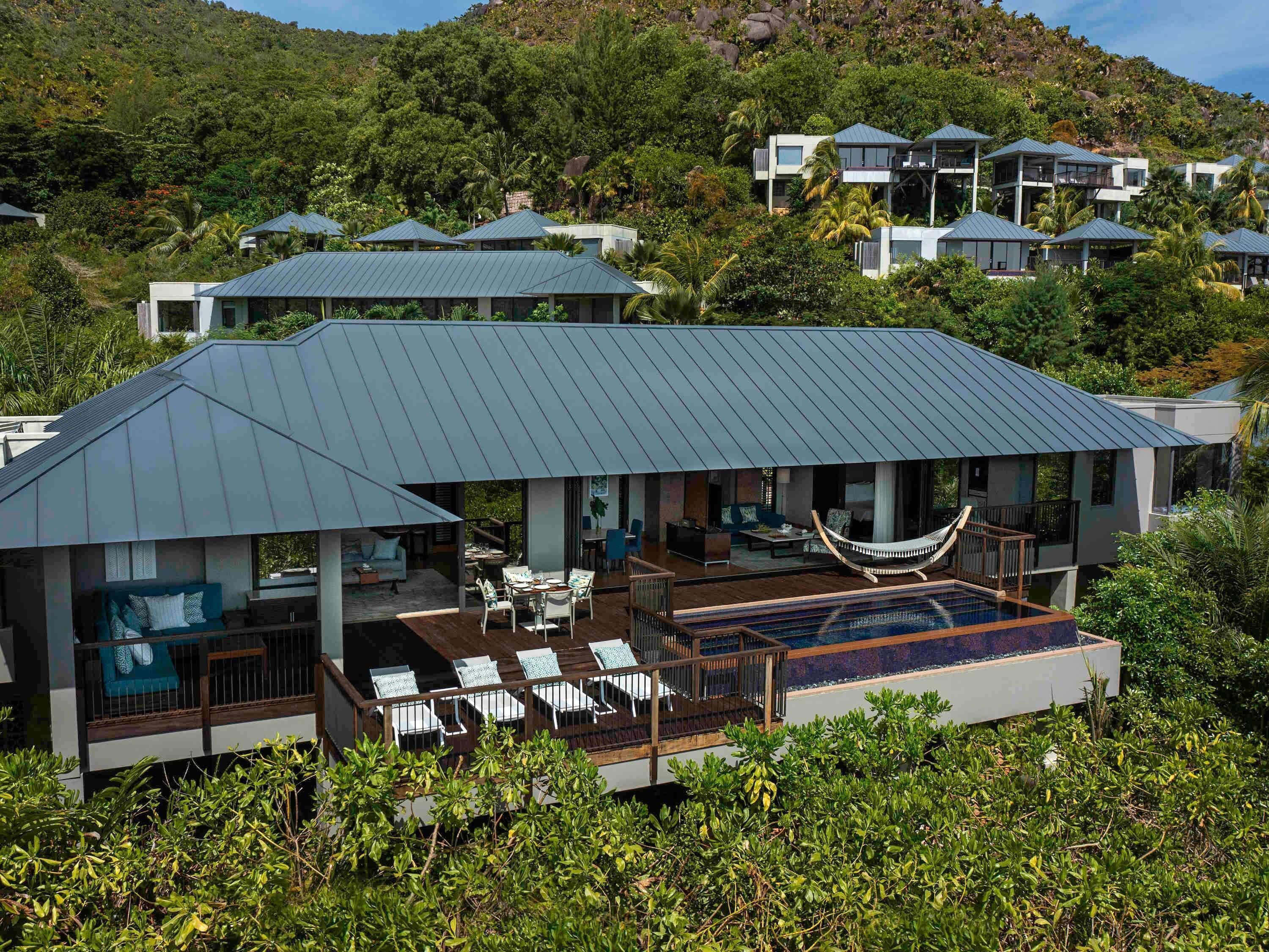 A modern villa with a large deck, outdoor seating, and a hammock.
