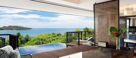 A modern living room with a view of the sea, a pool, and a dining area with a chessboard.
