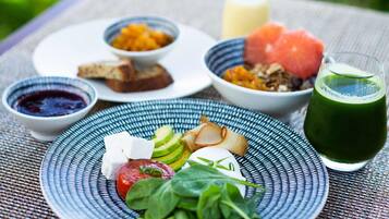 Comida con varios platos sobre una mesa, incluyendo un plato de verduras, un bol de fruta y un vaso de jugo verde.