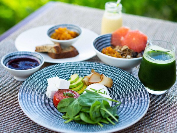 A meal with various dishes on a table, including a plate with vegetables, a bowl of fruit, and a glass of green juice.