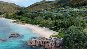 Un resort costero con villas frente a la playa, aguas turquesas cristalinas y exuberante vegetación.