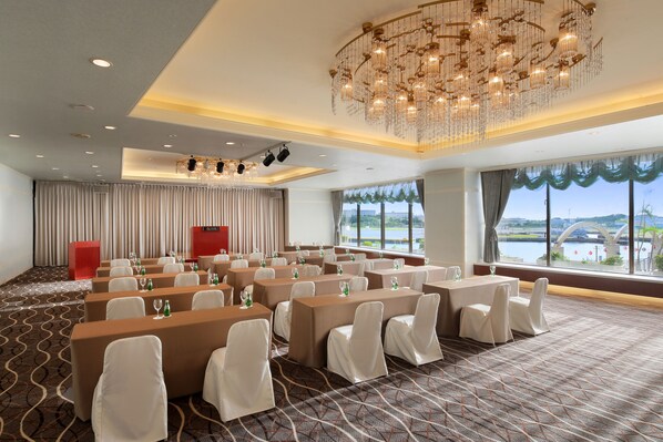 A conference room with tables and chairs, a chandelier, and a view of a body of water.