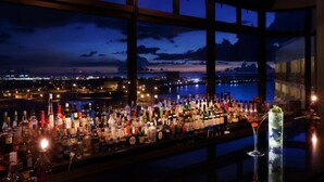 Eine Bar mit Blick auf die Stadt in der Dämmerung, mit einer Auswahl an Flaschen und einem Martini-Glas.
