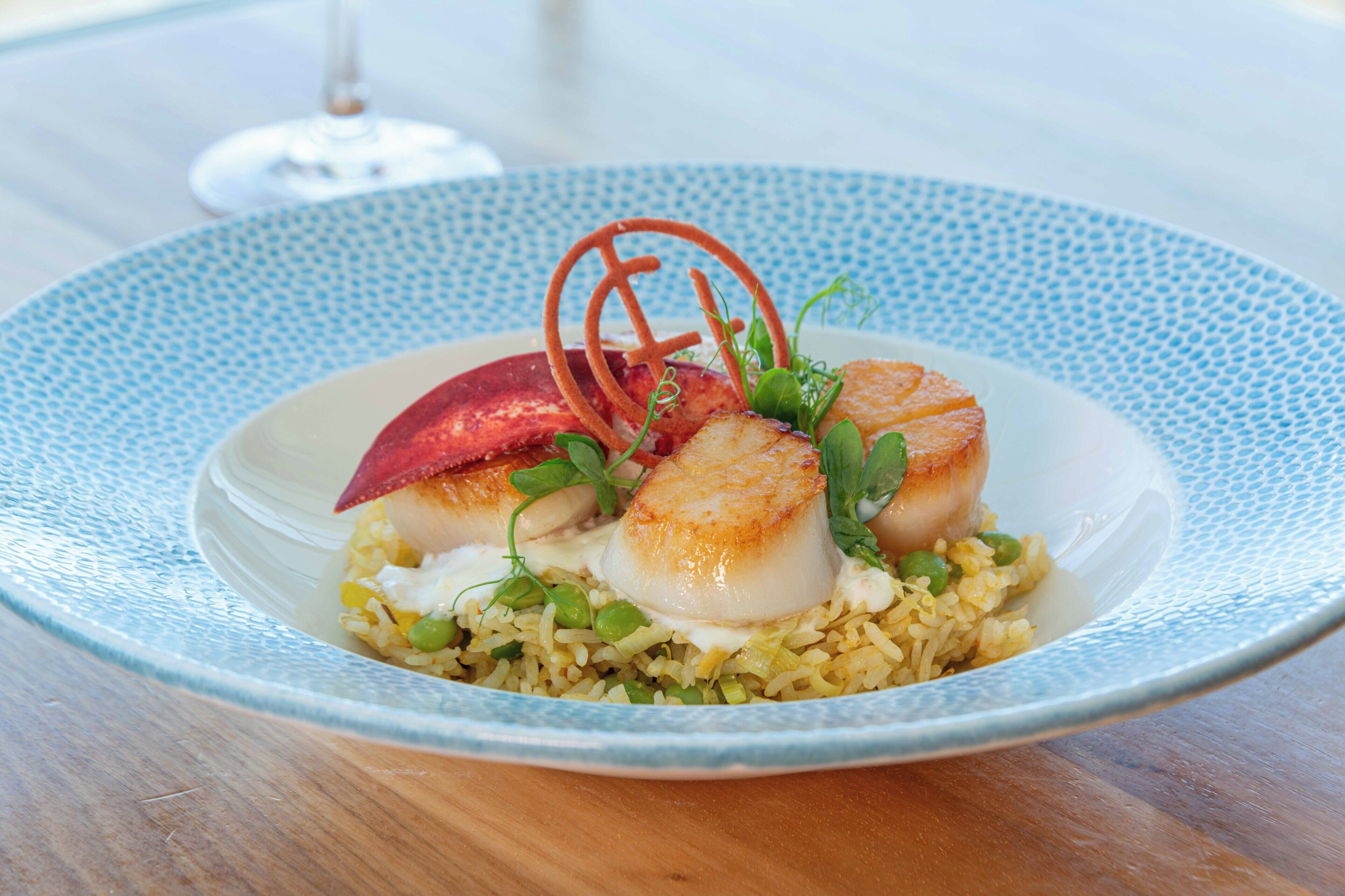 A plate of food with seared scallops, rice, peas, and garnishes on a blue patterned plate.