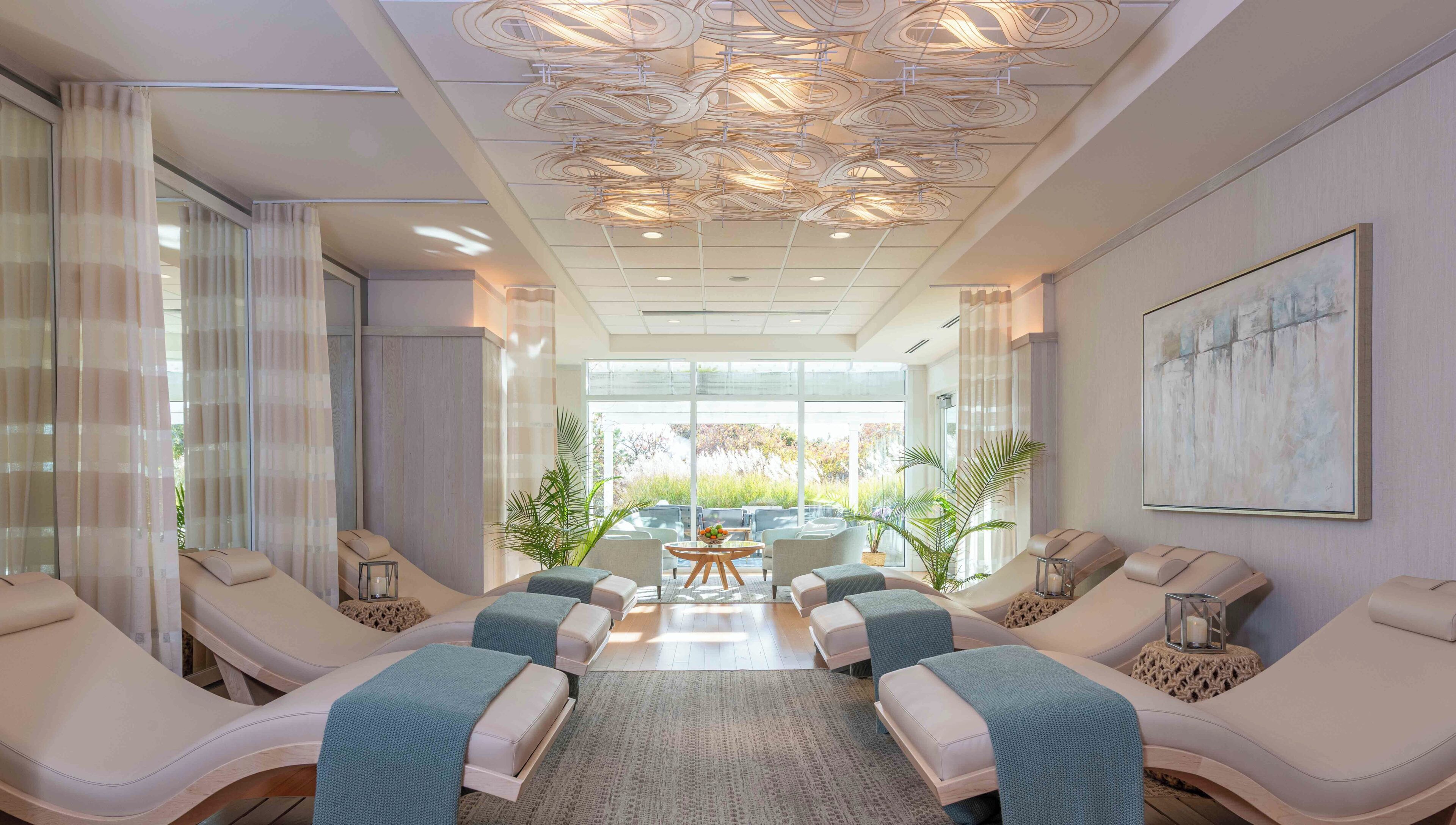 A spa room with reclining chairs, a massage table, and a large window with a view of the outdoors.