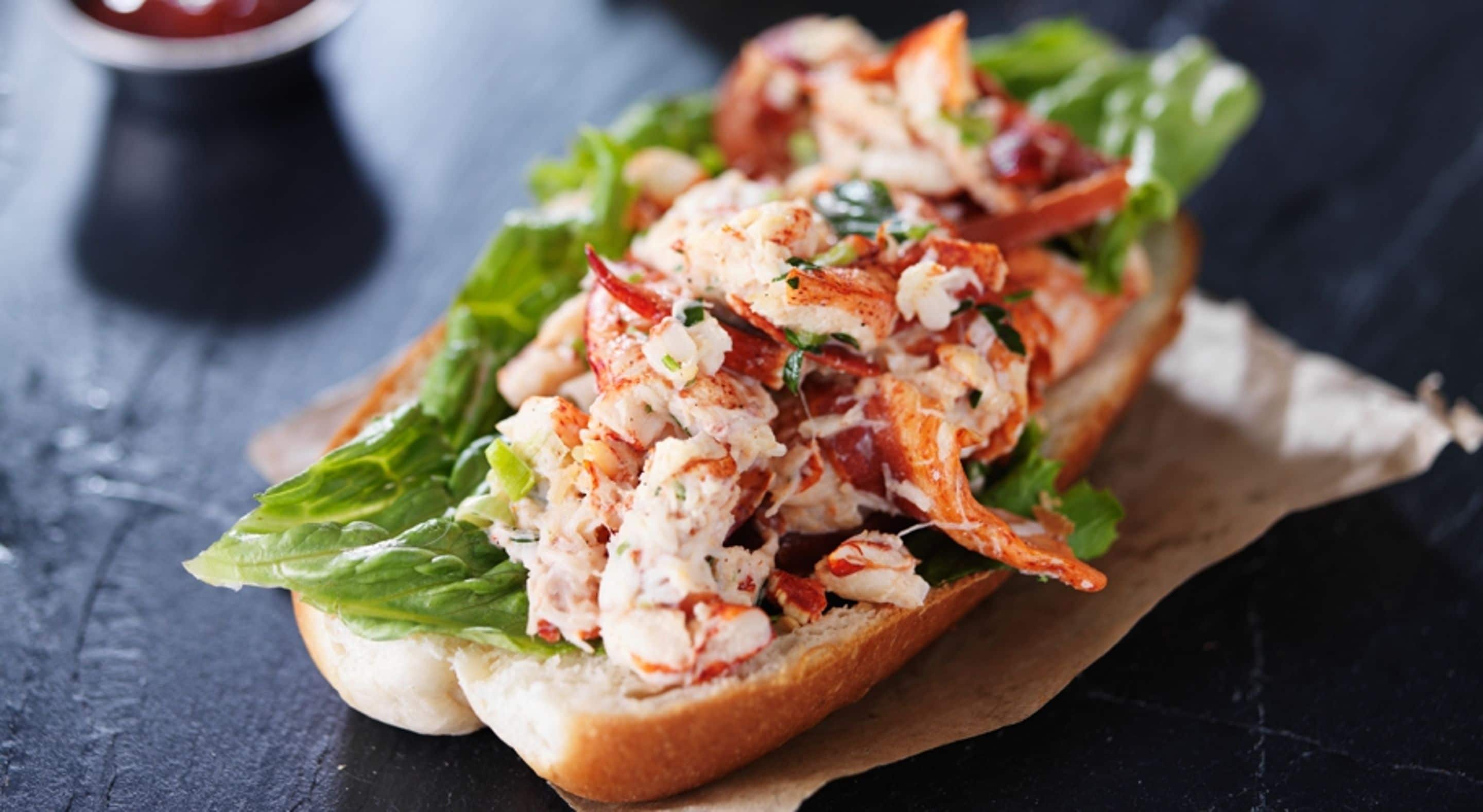 A lobster roll on a bun with lettuce and a side of ketchup.