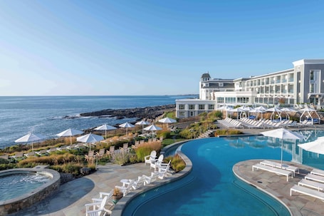 A resort with a pool, lounge chairs, umbrellas, and a view of the ocean.