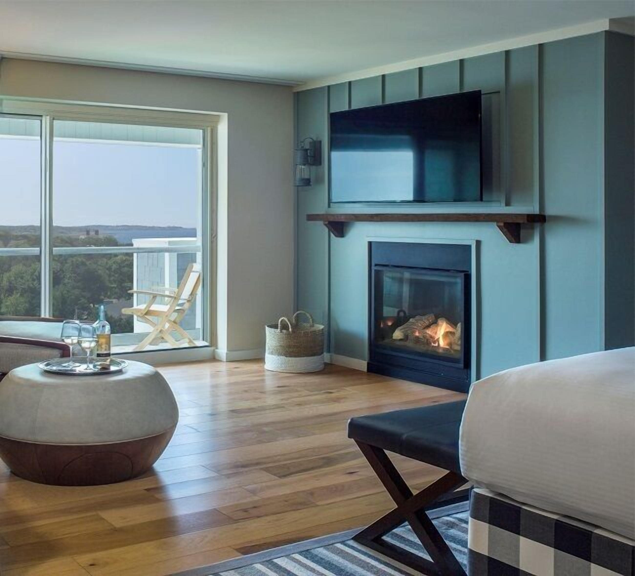 A modern living room with a fireplace, a large TV mounted above it, and a balcony with a view.