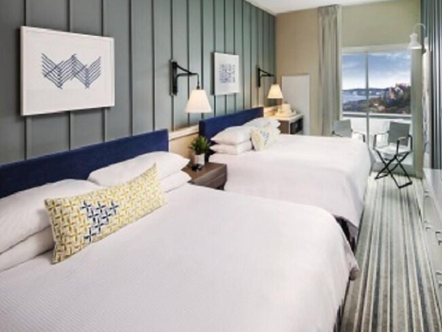 Habitación de hotel con dos camas, un ventanal grande y vistas a la ciudad.