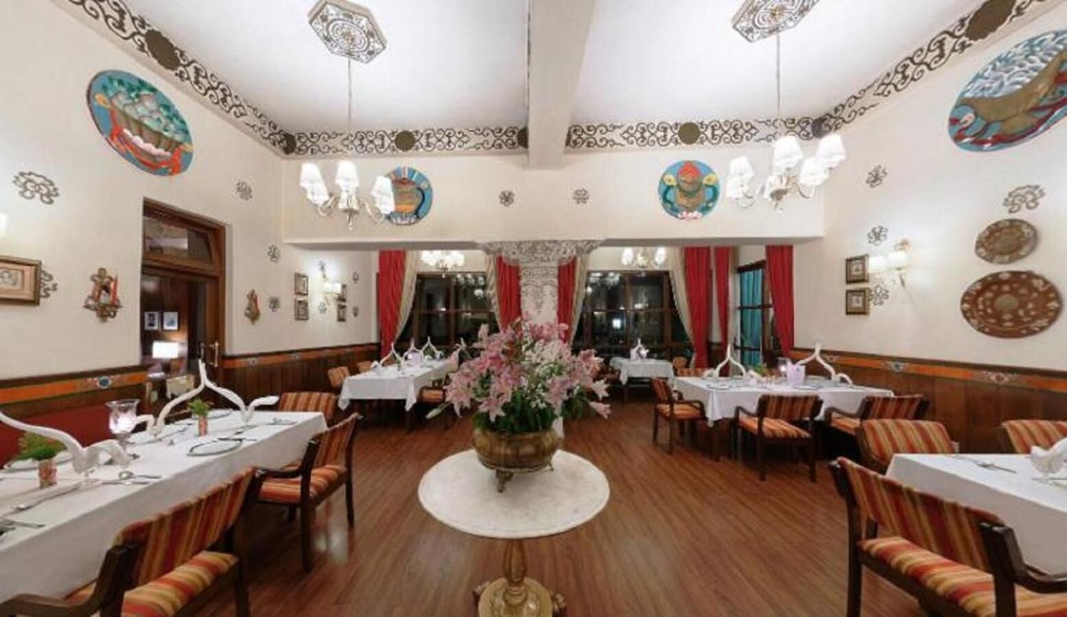 A formal dining room with round tables, chairs, and a central floral arrangement.