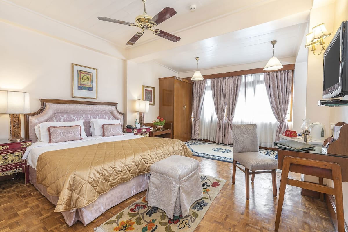 A hotel room with a bed, desk, chair, ceiling fan, and a large window with curtains.