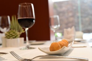 Une table à manger avec une assiette blanche remplie de croquettes, un verre de vin rouge et une bougie.