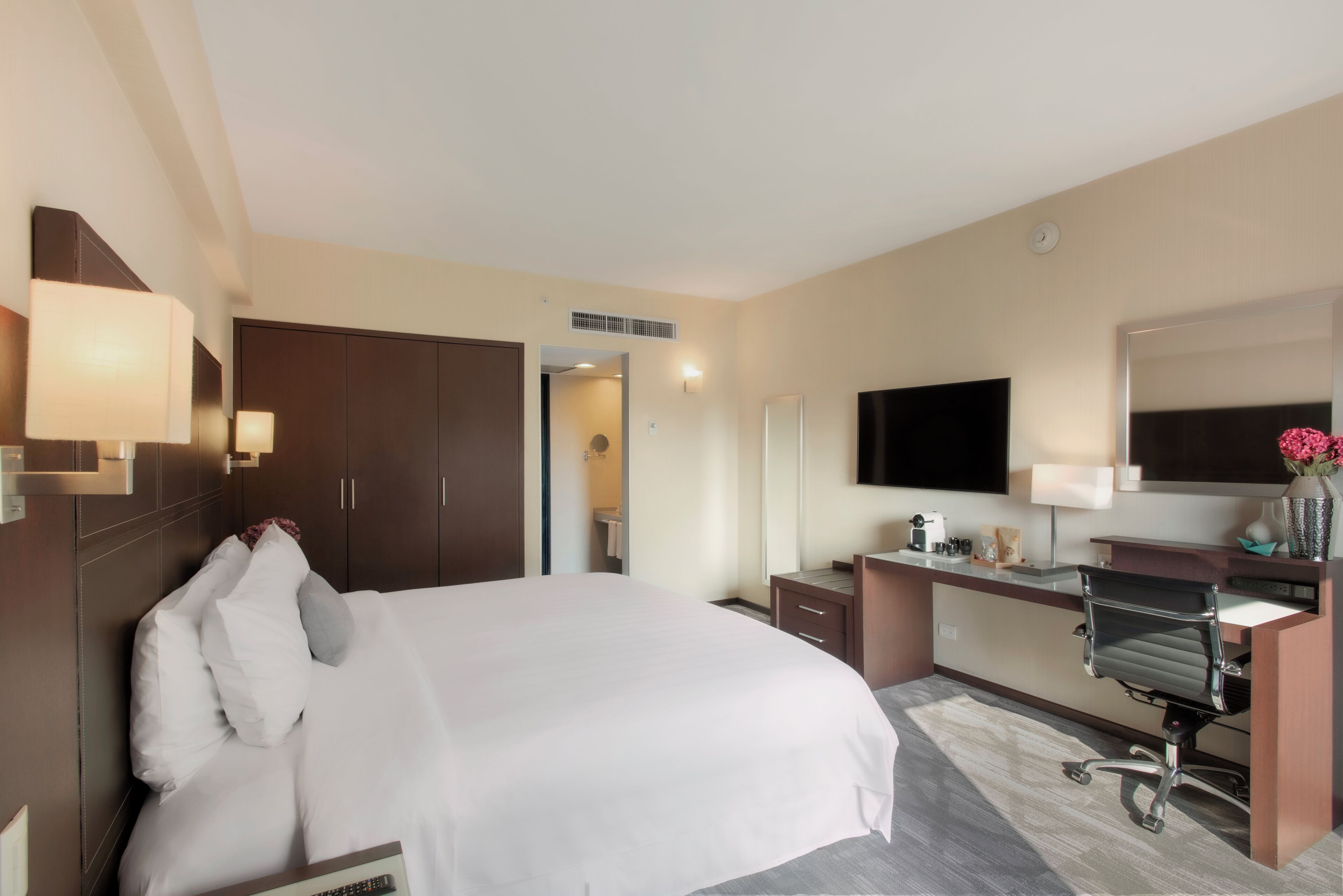 A hotel room with a large bed, a desk with a chair, a flat-screen TV, and a mirror.