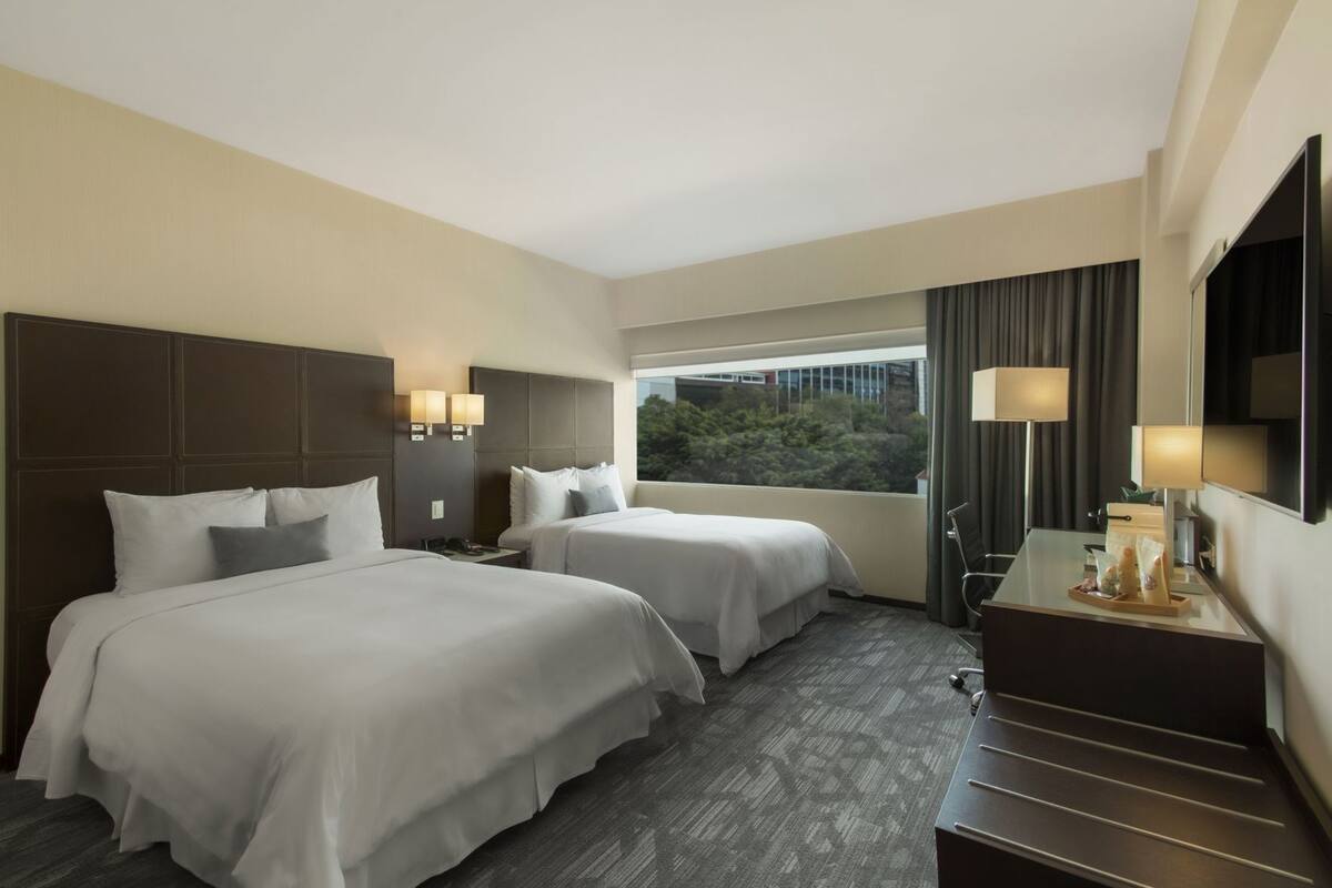 A hotel room with two beds, a desk, a chair, and a large window.