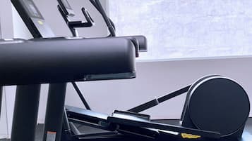 Uma bicicleta ergométrica com visor digital, um espelho fixado na parede e uma janela com vista para a cidade.