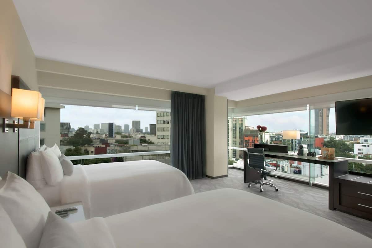 A hotel room with two beds, a desk, a chair, a TV, and a city view.