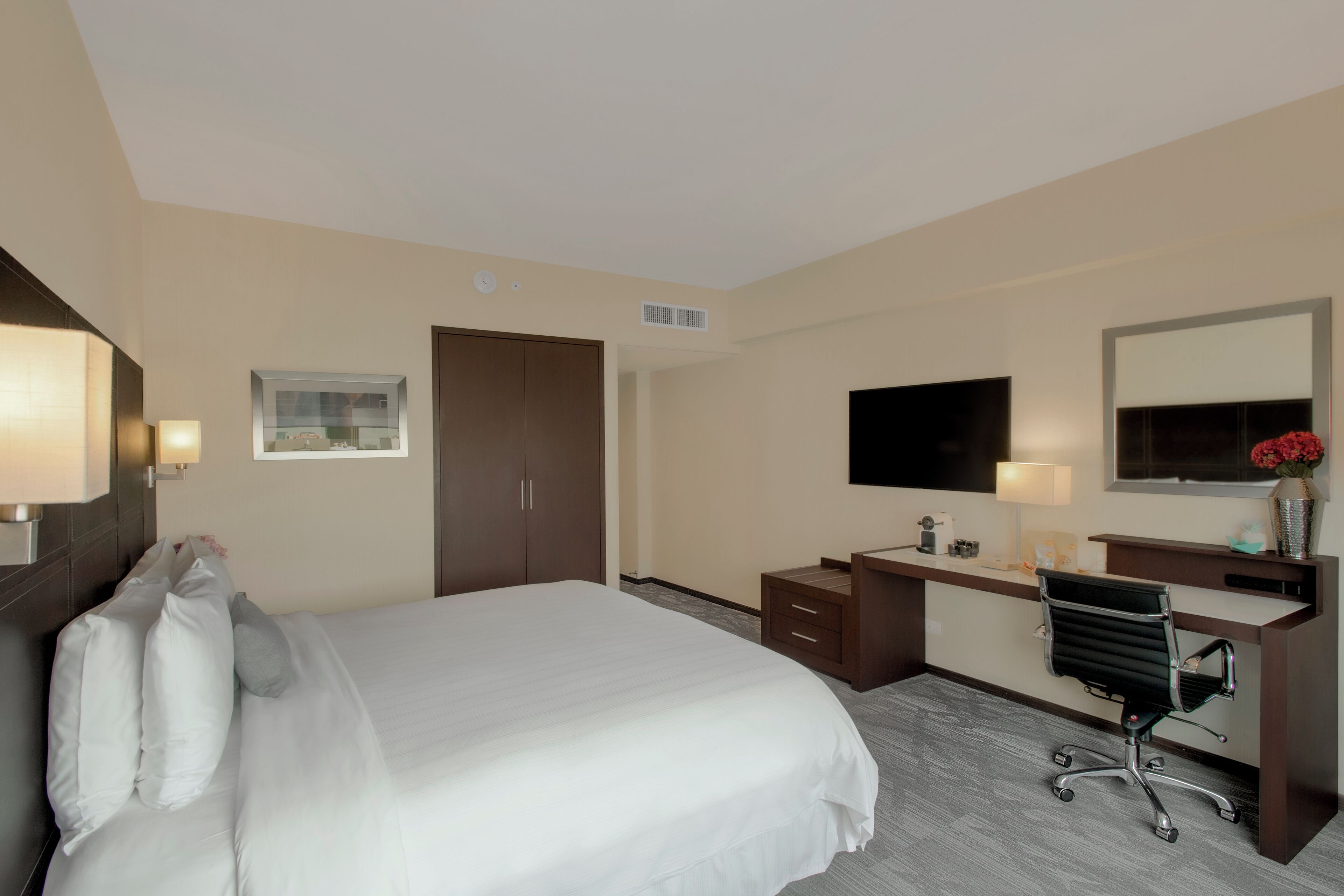 A hotel room with a large bed, a desk with a chair, a television, and a mirror.