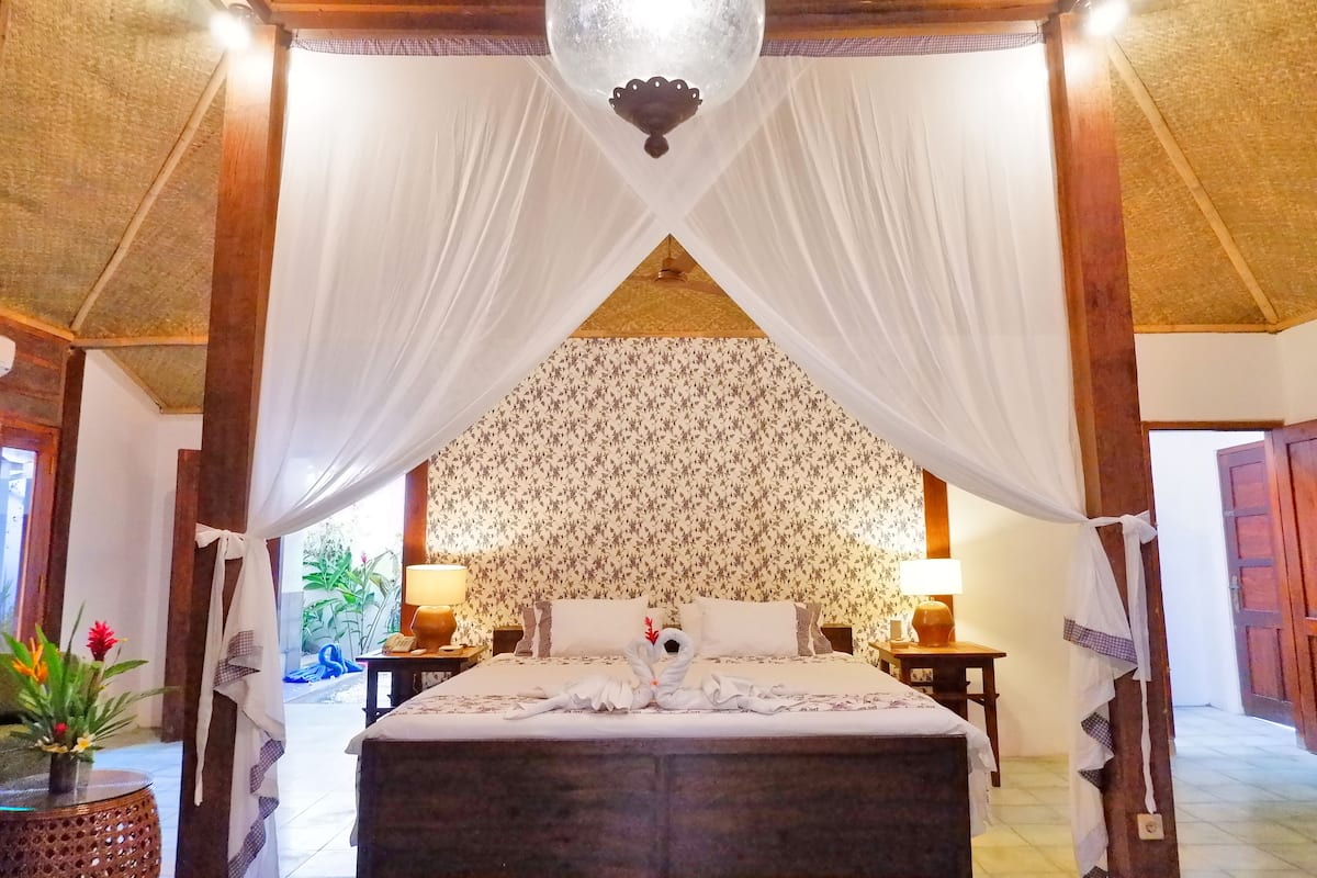 A room with a bed, a canopy, a patterned wall, and a wooden ceiling.