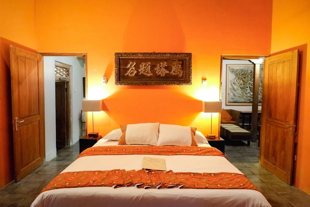 A hotel room with a large bed, two bedside lamps, a wooden door, and a framed artwork on the wall.