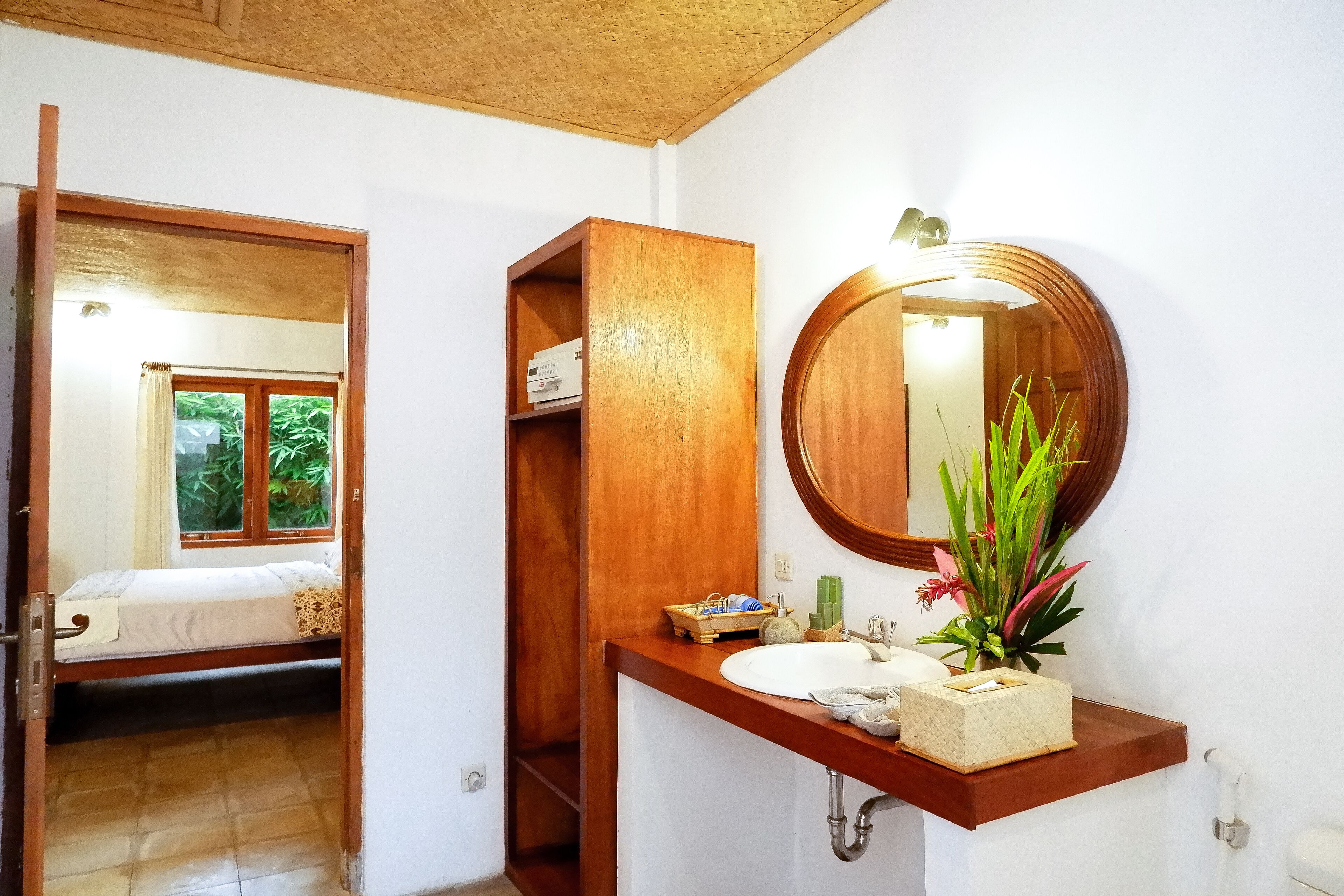 Un baño con tocador de madera, un espejo redondo y una ventana con cortinas.