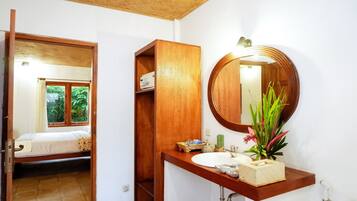 Un baño con tocador de madera, un espejo redondo y una ventana con cortinas.