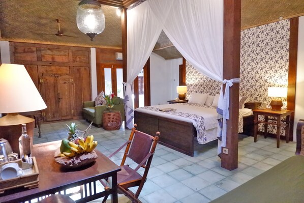 A room with a bed, a table with fruits, a chair, a lamp, and a decorative plant. - d'Omah Hotel Yogya (Sewon)