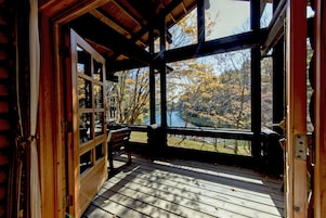 Una cabaña de madera con terraza, ventanas amplias y vistas a árboles otoñales.