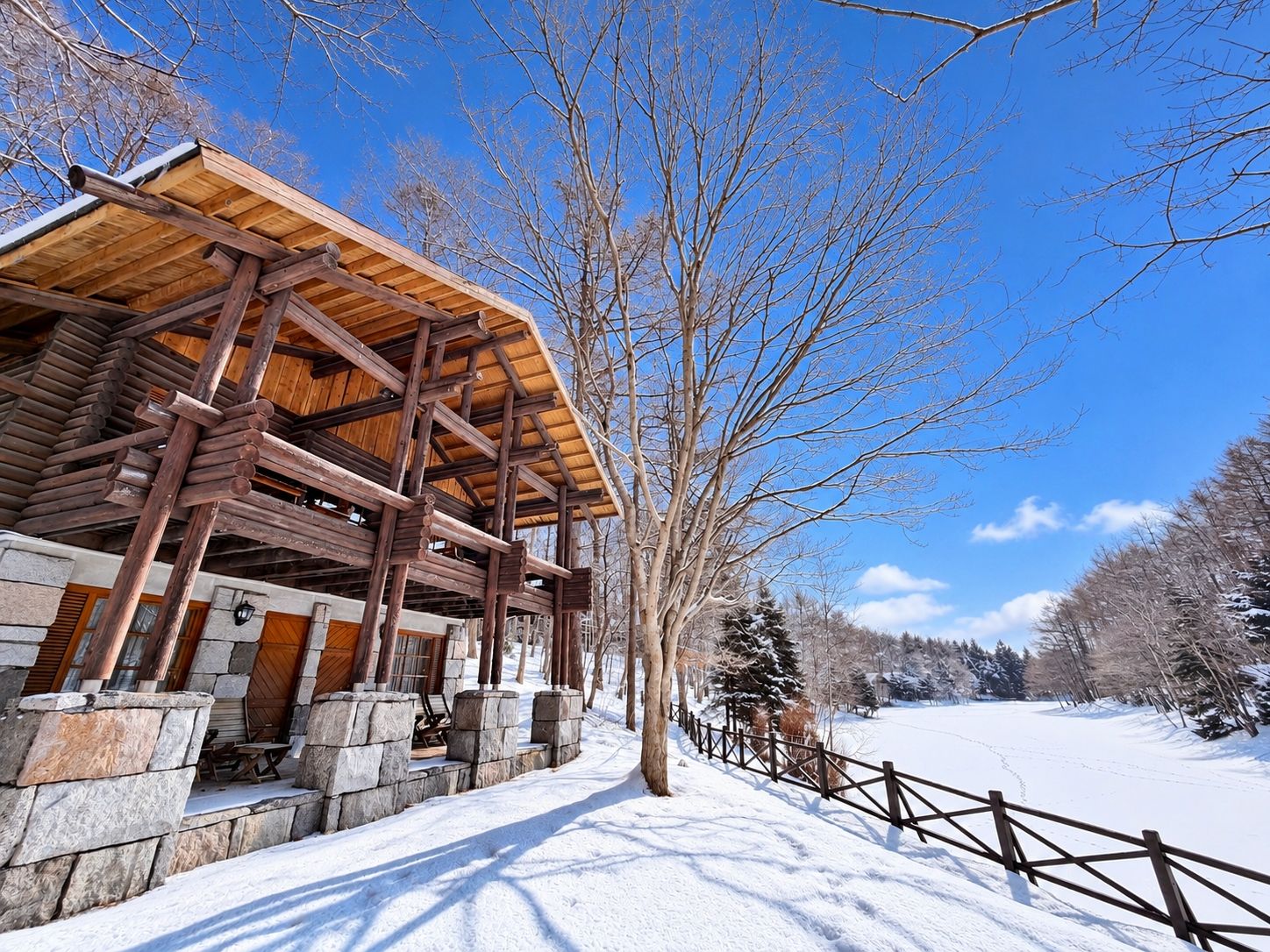 A wooden cabin with a stone foundation, a wooden deck, and a snow-covered landscape.