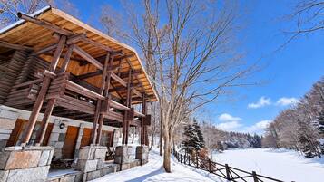 Une cabane en bois avec des fondations en pierre, une terrasse en bois et un paysage enneigé.