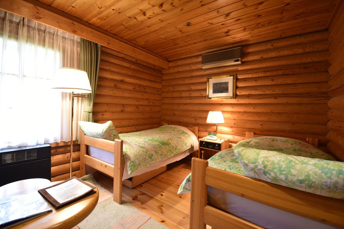 A cabin room with two wooden beds, a table, a lamp, and a framed picture on the wall.