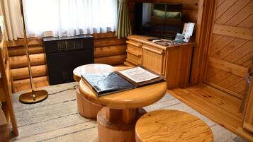 A cozy cabin-style room with a wooden interior, a small kitchenette, a television, and a dining area with a table and stools.