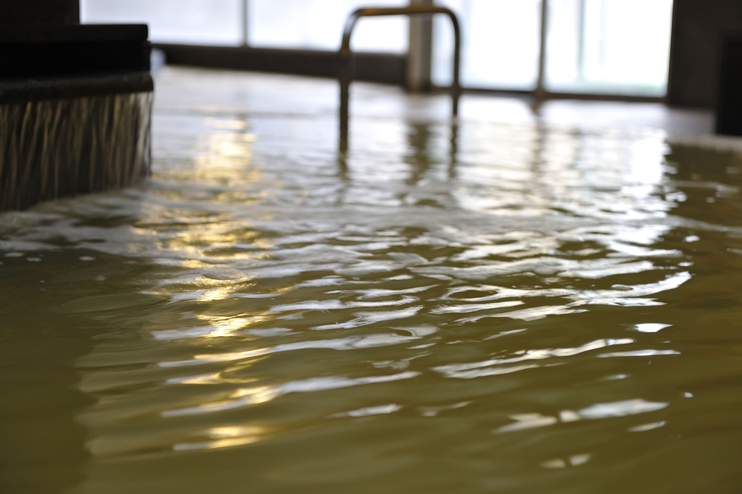 Piso mojado con reflejos de luz, una silla y una ventana al fondo.