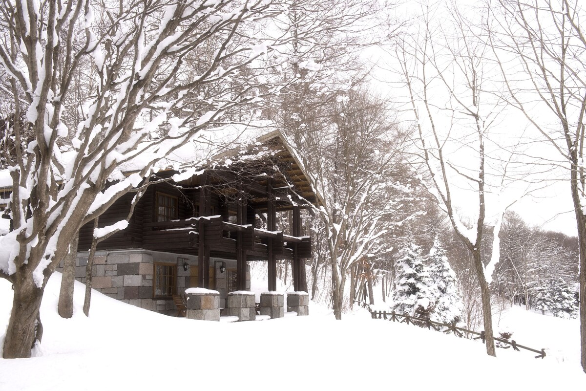 Eine Blockhütte mit Steinmauern und einer Holzterrasse, umgeben von schneebedeckten Bäumen.