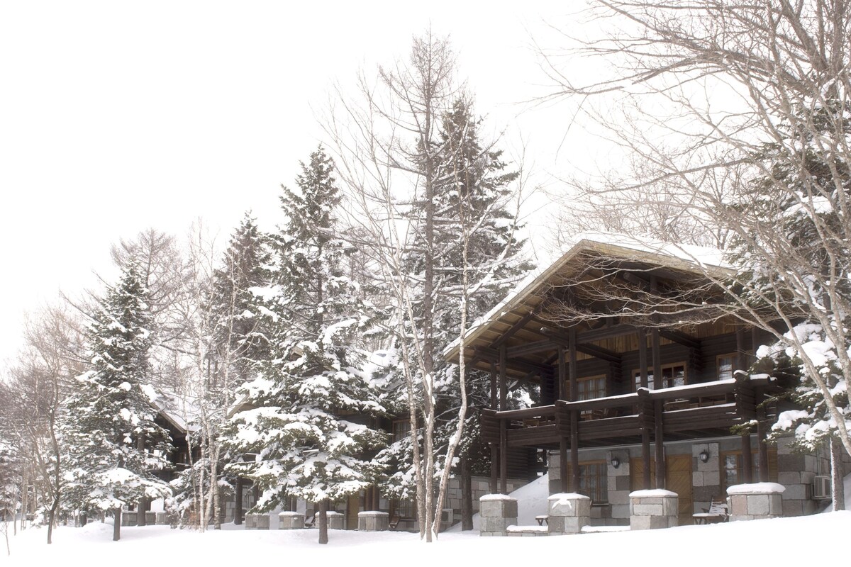 Eine Holzhütte mit einer Holzterrasse, umgeben von schneebedeckten Bäumen.