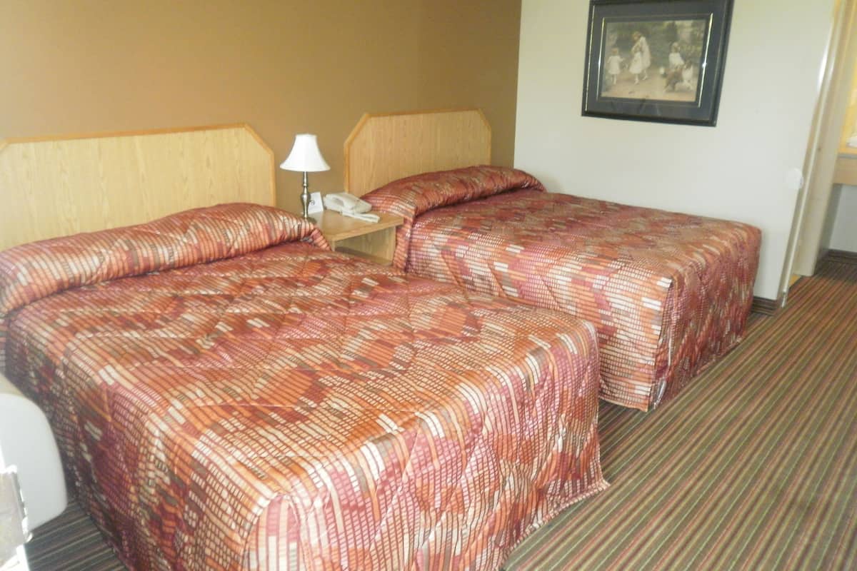 Habitación de hotel con dos camas, una mesita de noche, una lámpara y un cuadro en la pared.