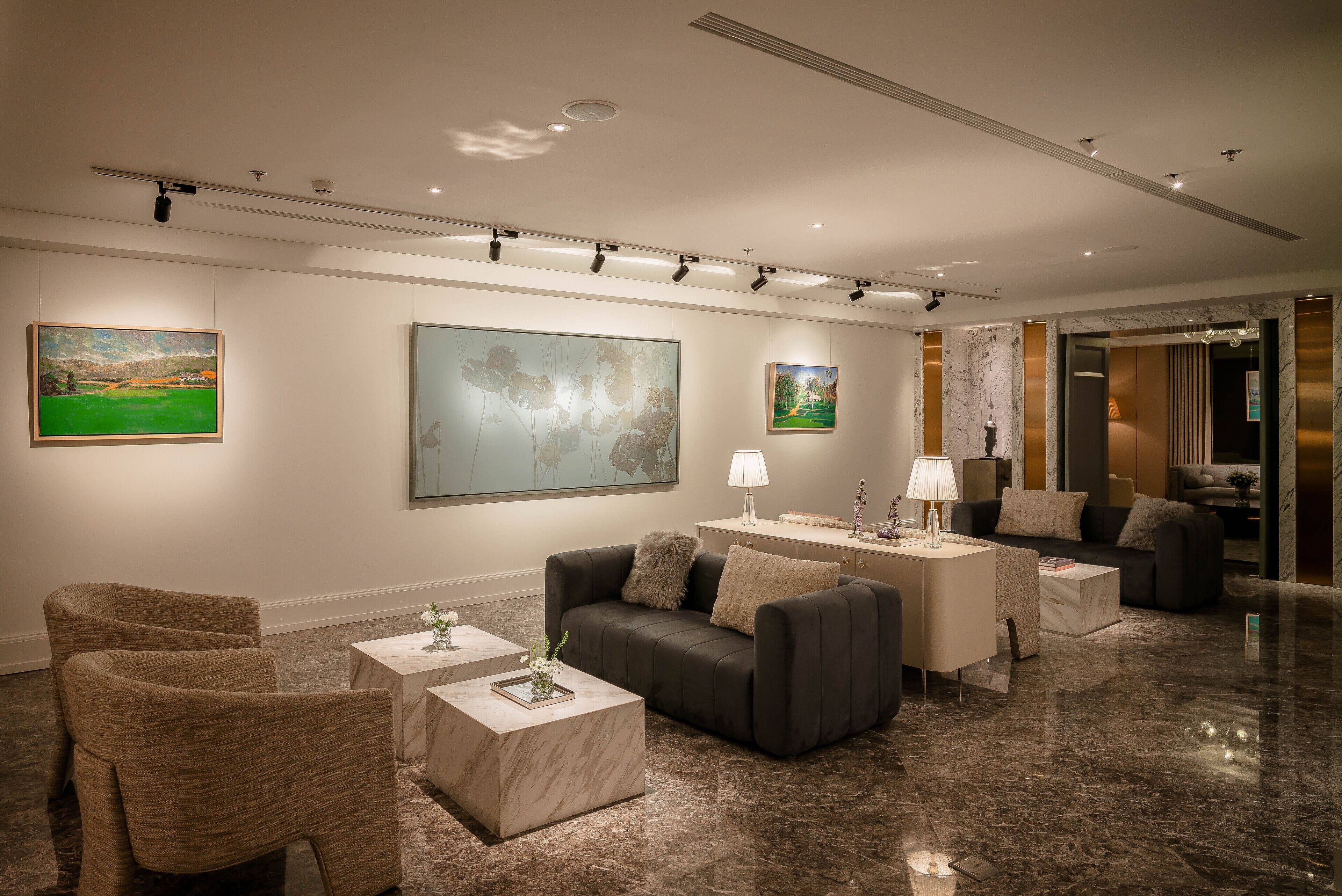 A modern hotel lobby with a marble floor, a grey sofa, a coffee table, and a side table with a lamp.