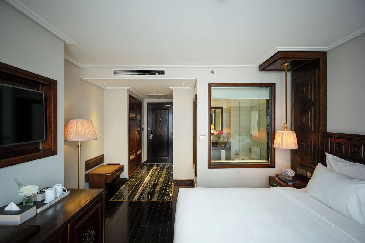 A hotel room with a bed, bedside table, lamp, TV, and a mirror.