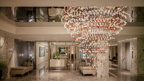 Een ruime lobby met een hoog plafond, marmeren vloeren en een grote kroonluchter in het midden.