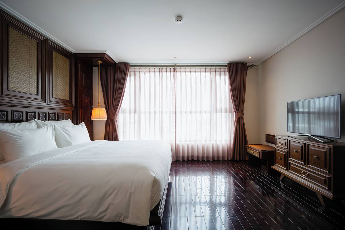 A hotel room with a large bed, a desk, a television, and a window with curtains.