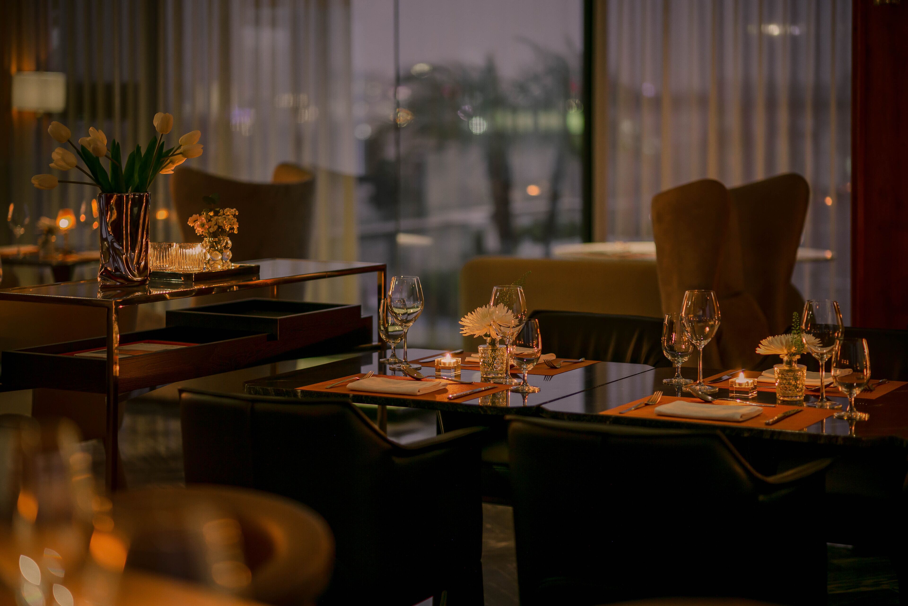A dining area with tables set for two, featuring candles and floral centerpieces.