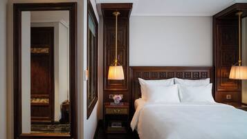 Una habitación de hotel con una cama grande, una mesita de noche con lámpara, un espejo y un cabecero de madera.