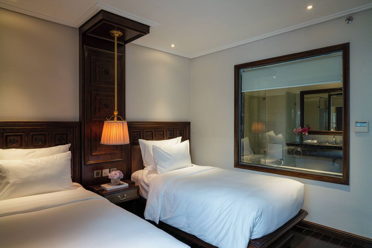 A hotel room with two beds, a nightstand, a lamp, and a large mirror.