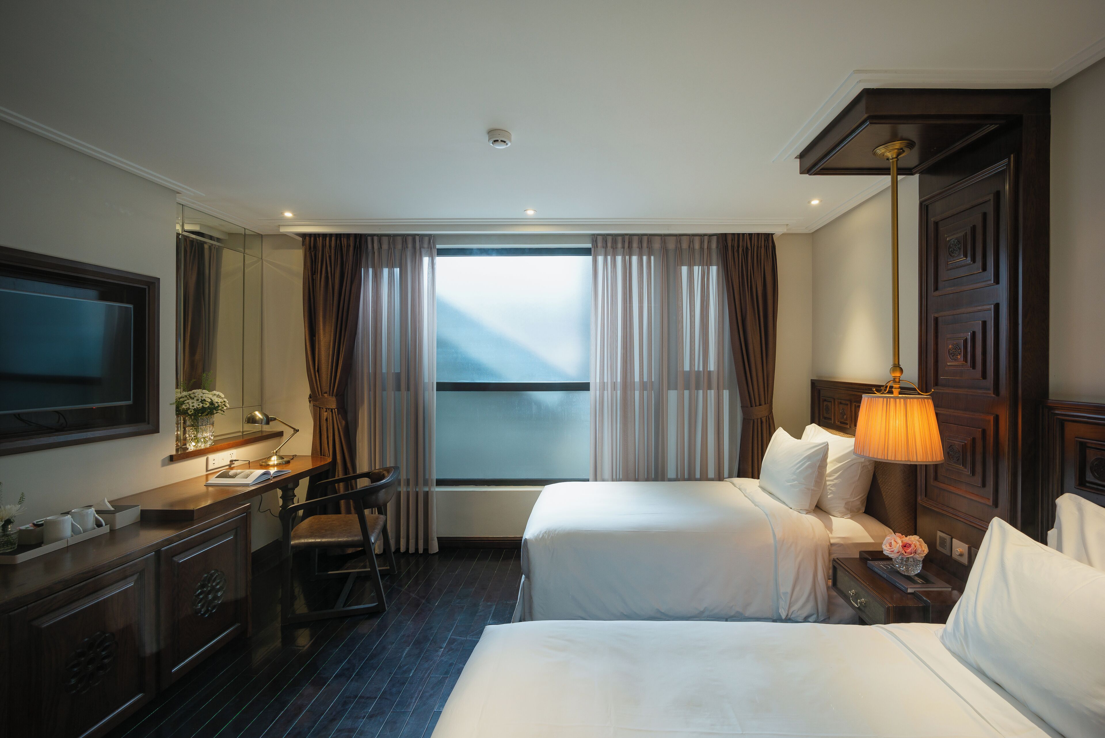 Ein Hotelzimmer mit einem großen Bett, einem Schreibtisch mit Stuhl, einem Fernseher und einem Fenster mit Vorhängen.